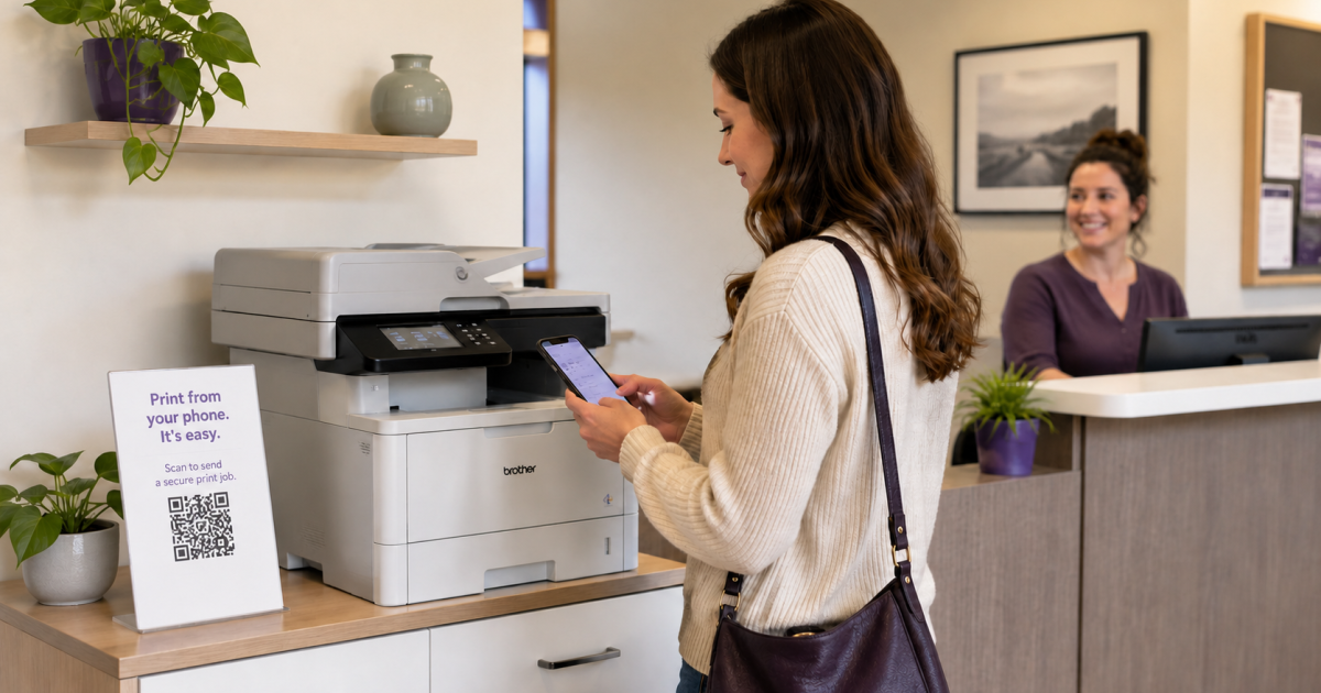 A visitor stands at an office credenza scanning a QR code on a "Print from your phone" sign next to a Brother printer, while a receptionist watches from the desk behind.